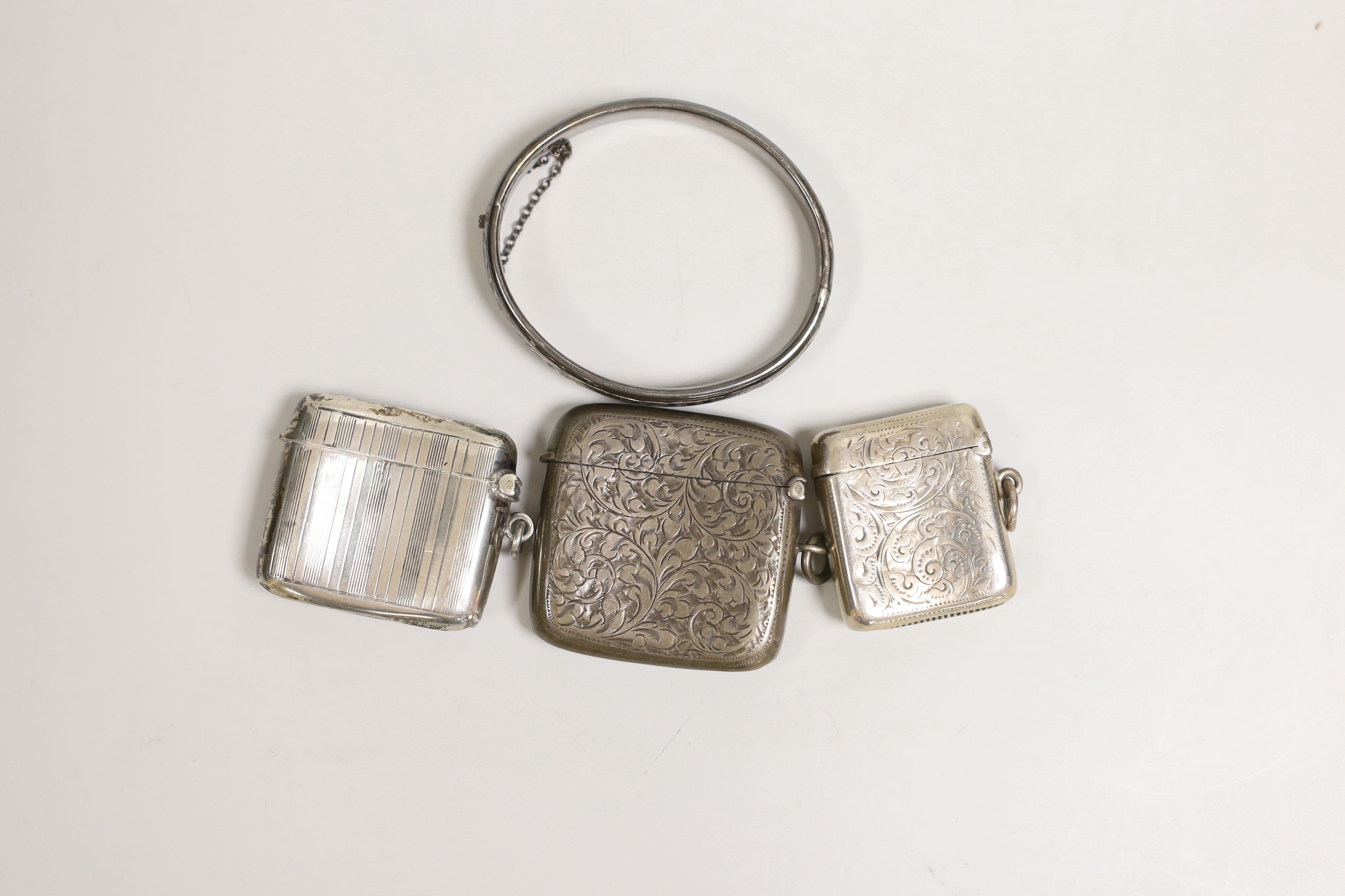 Three assorted late 19th/early 20th century chased silver vesta cases and a chased silver hinged bangle.